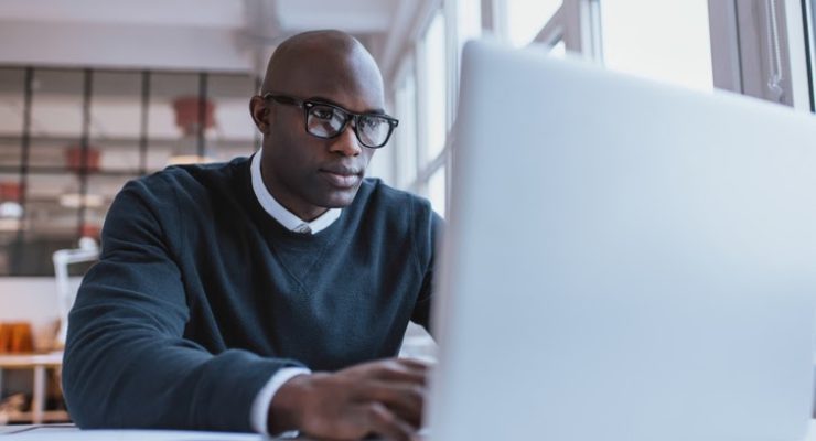 Young businessman working on his laptop in office. Young african executive sitting at his desk surfing internet on laptop computer.